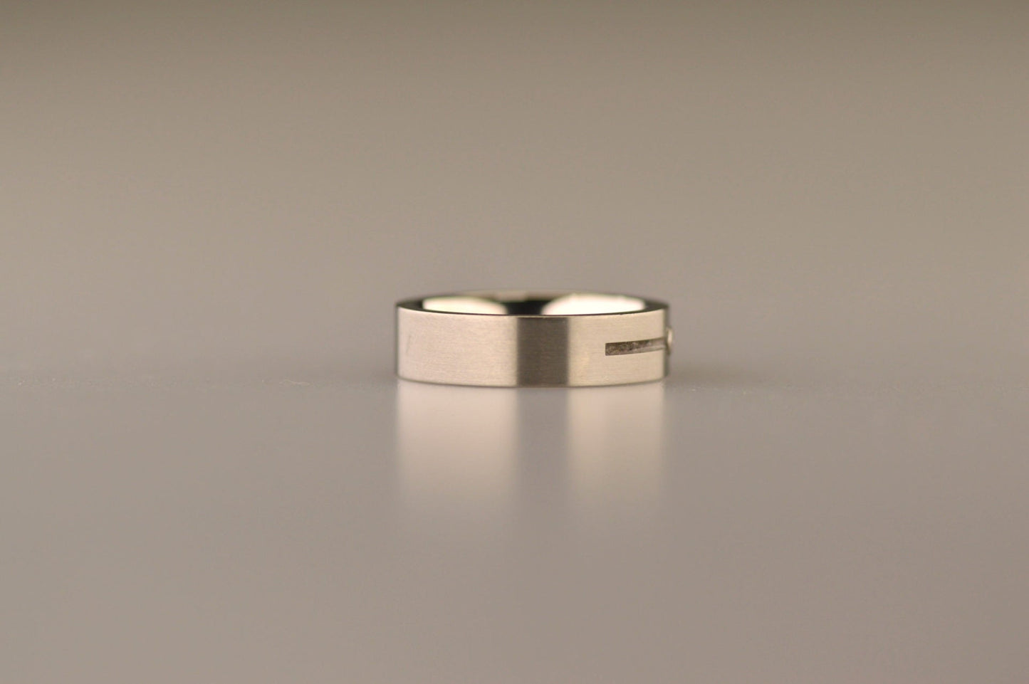 Ring als gedenksieraad 6 mm breed met één langwerpige streep, onderbroken door een zirkonia of diamant naar keuze, waardoor er twee compartimenten ontstaan, waar as of haar in verwerkt wordt. Alle
