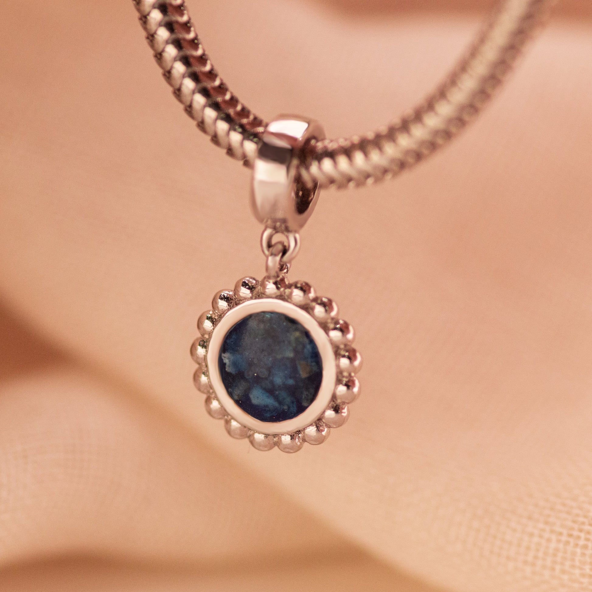 Asbedel met subtiel design die aan de voorzijde zichtbaar gevuld wordt met as of haar. Het vullen en sealen wordt in onze ambachtelijke edelsmederij gedaan. Gedenksieraad.alle