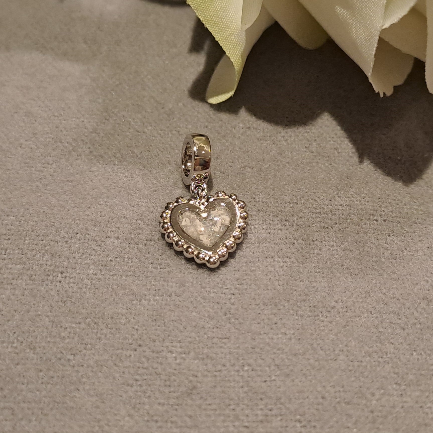 Hartvormige asbedel met subtiel design, die aan de voorzijde zichtbaar gevuld wordt met as of haar. Het herinneringssieraad. Alle