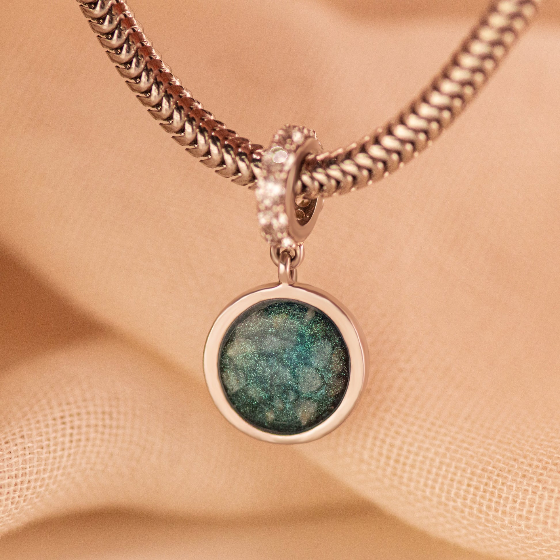 Asbedel rond subtiel design , het hangoog aan de buitenrand afgewerkt met zirkonia's, die aan de voorzijde zichtbaar gevuld wordt met as of haar met een keuze in 20 kleuren. Alle