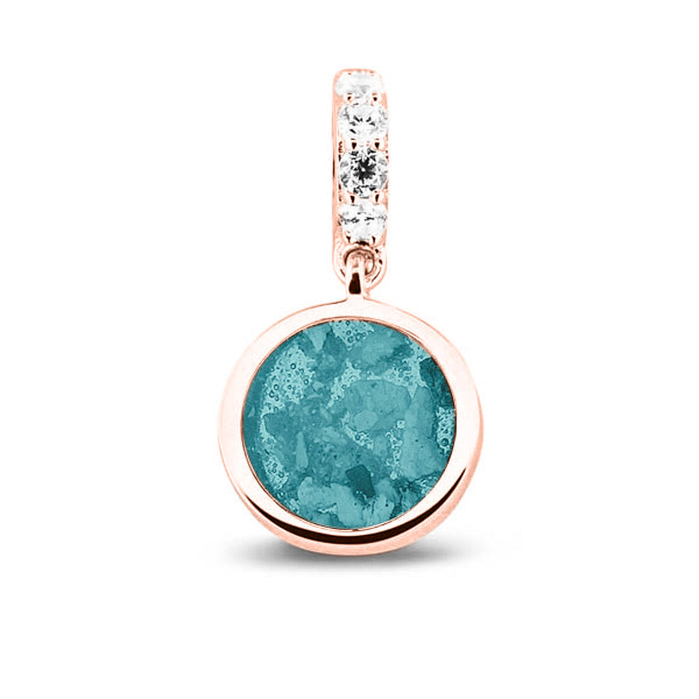 Asbedel rond subtiel design , het hangoog aan de buitenrand afgewerkt met zirkonia's, die aan de voorzijde zichtbaar gevuld wordt met as of haar met een keuze in 20 kleuren. Aqua