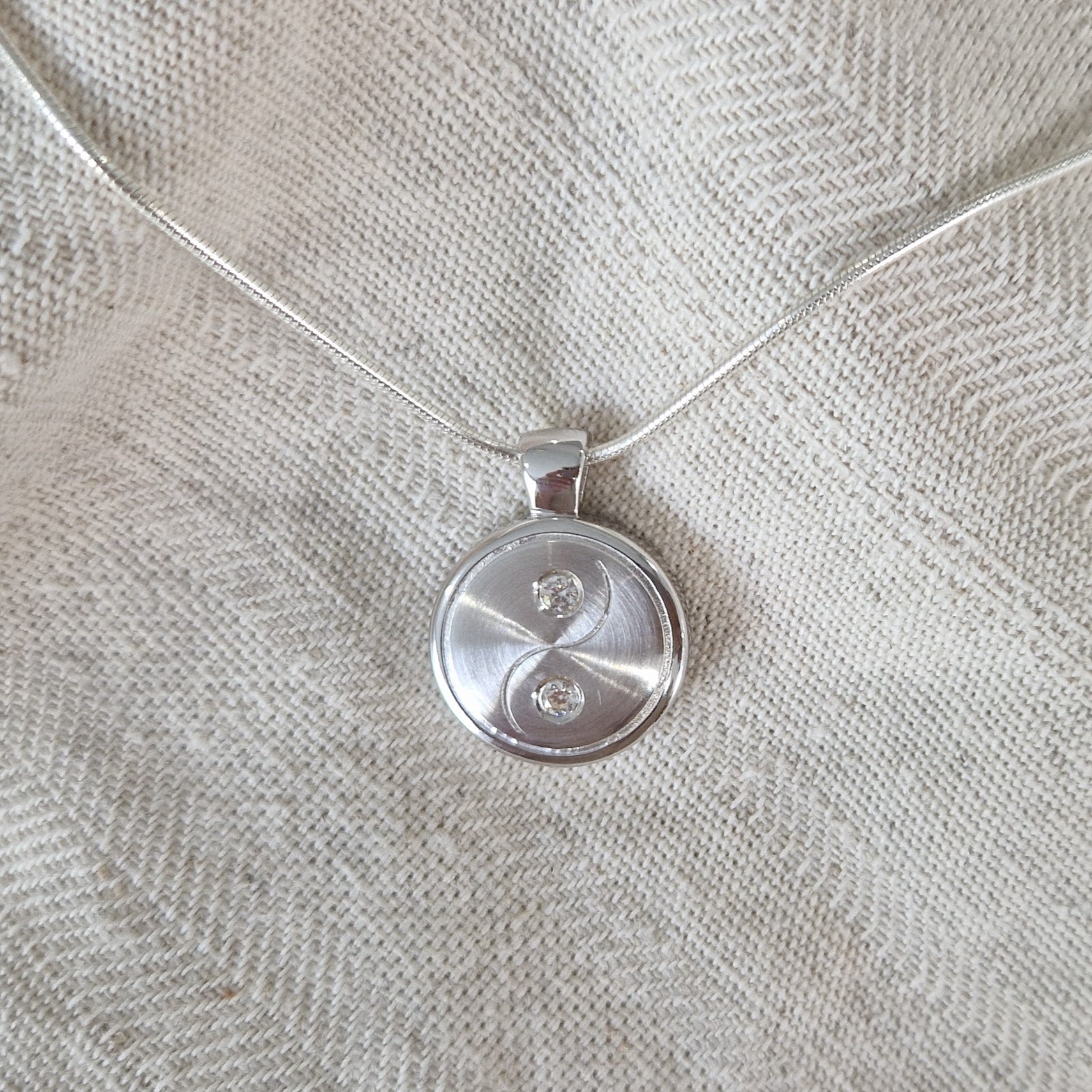 Yin yang hanger, dit sieraad beschikt over 2 askamers. In zilver uitgevoerd met zirkonia's, in goud met diamanten. Alle