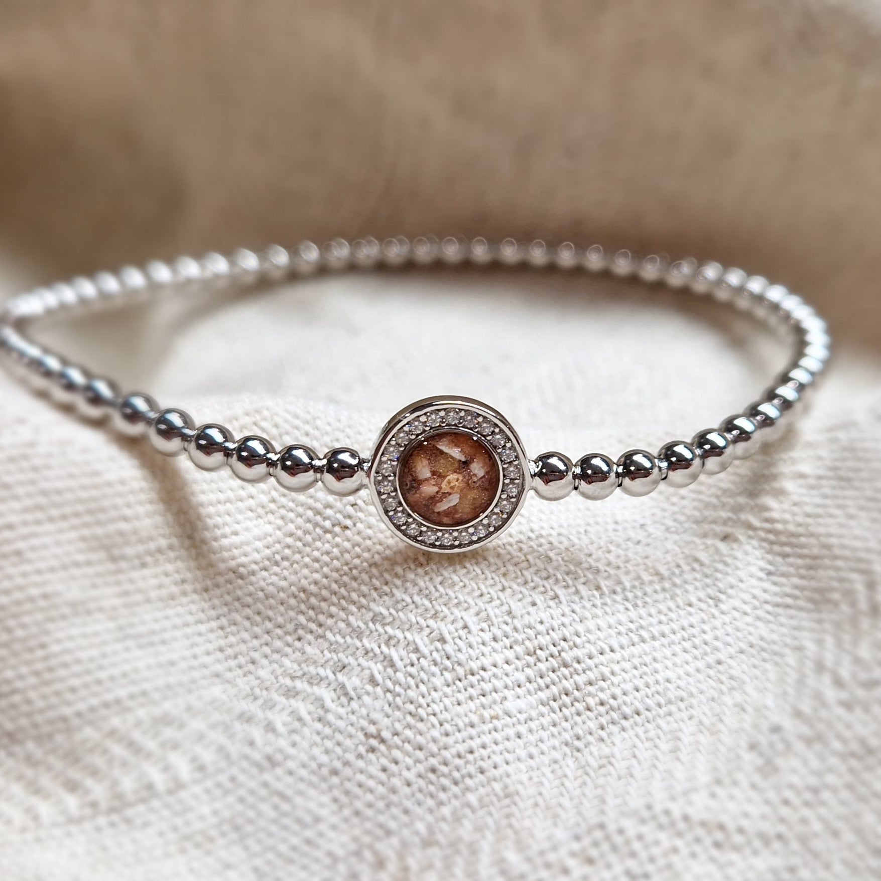 Flexibele as armband met rondje als compartiment gezet rondom met zirconia's voor as of haar. Alle