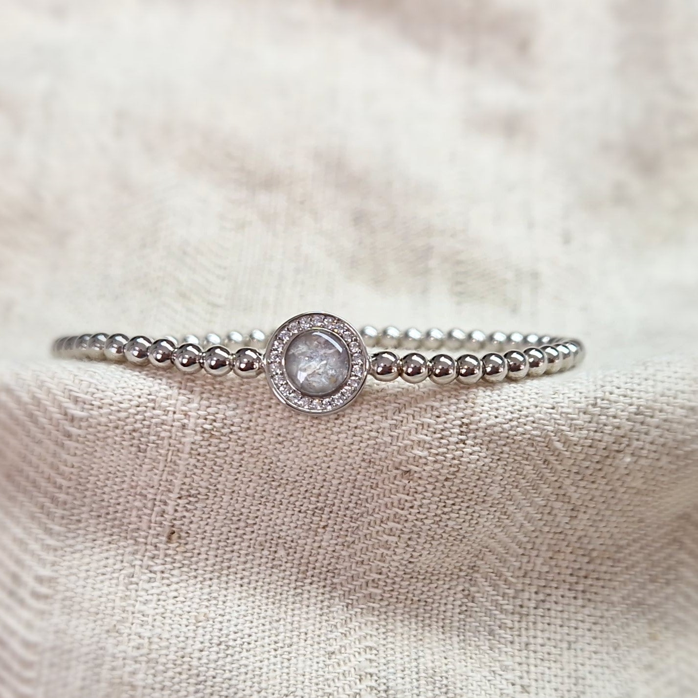 Flexibele as armband met rondje als compartiment gezet rondom met zirconia's voor as of haar. Alle