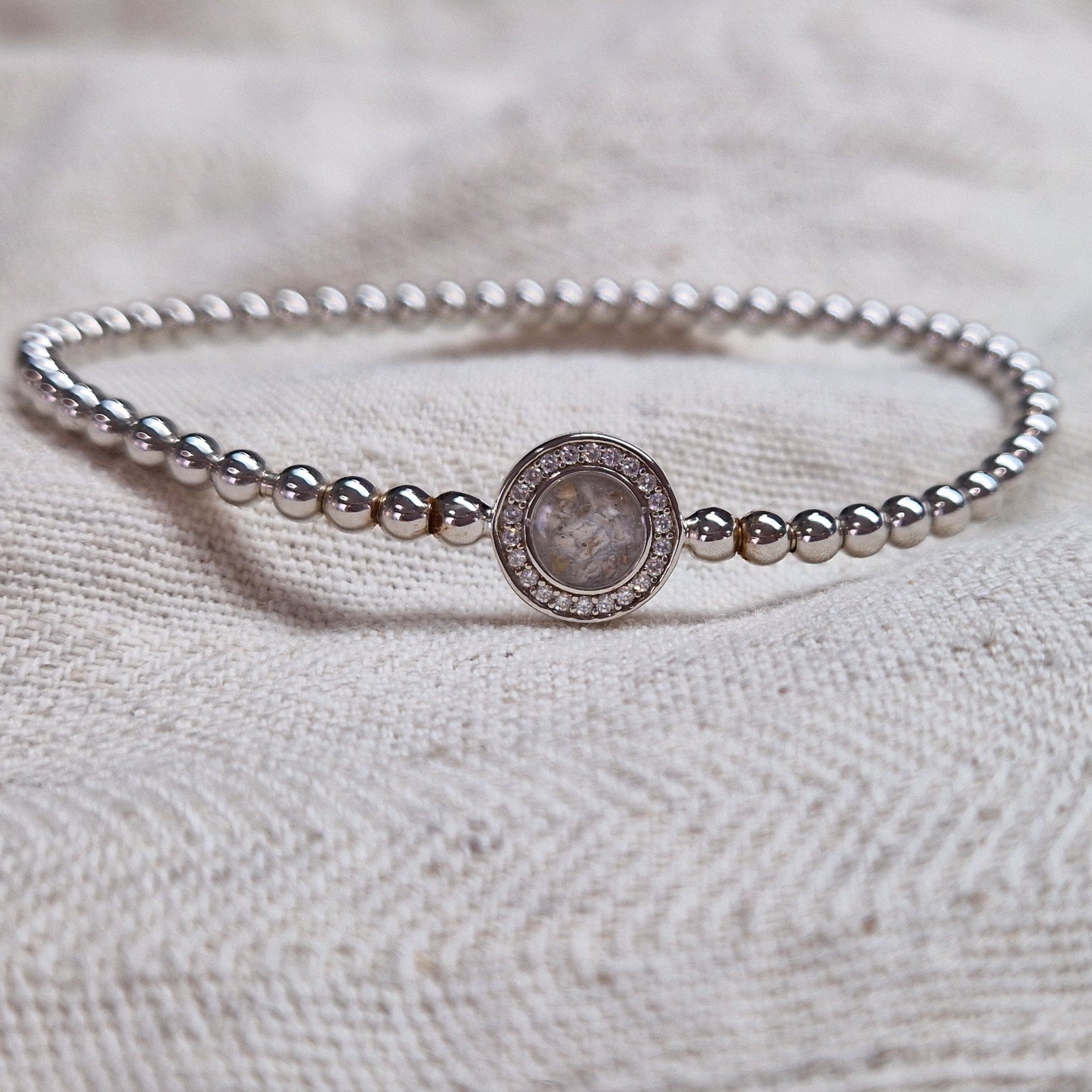 Flexibele as armband met rondje als compartiment gezet rondom met zirconia's voor as of haar. Alle