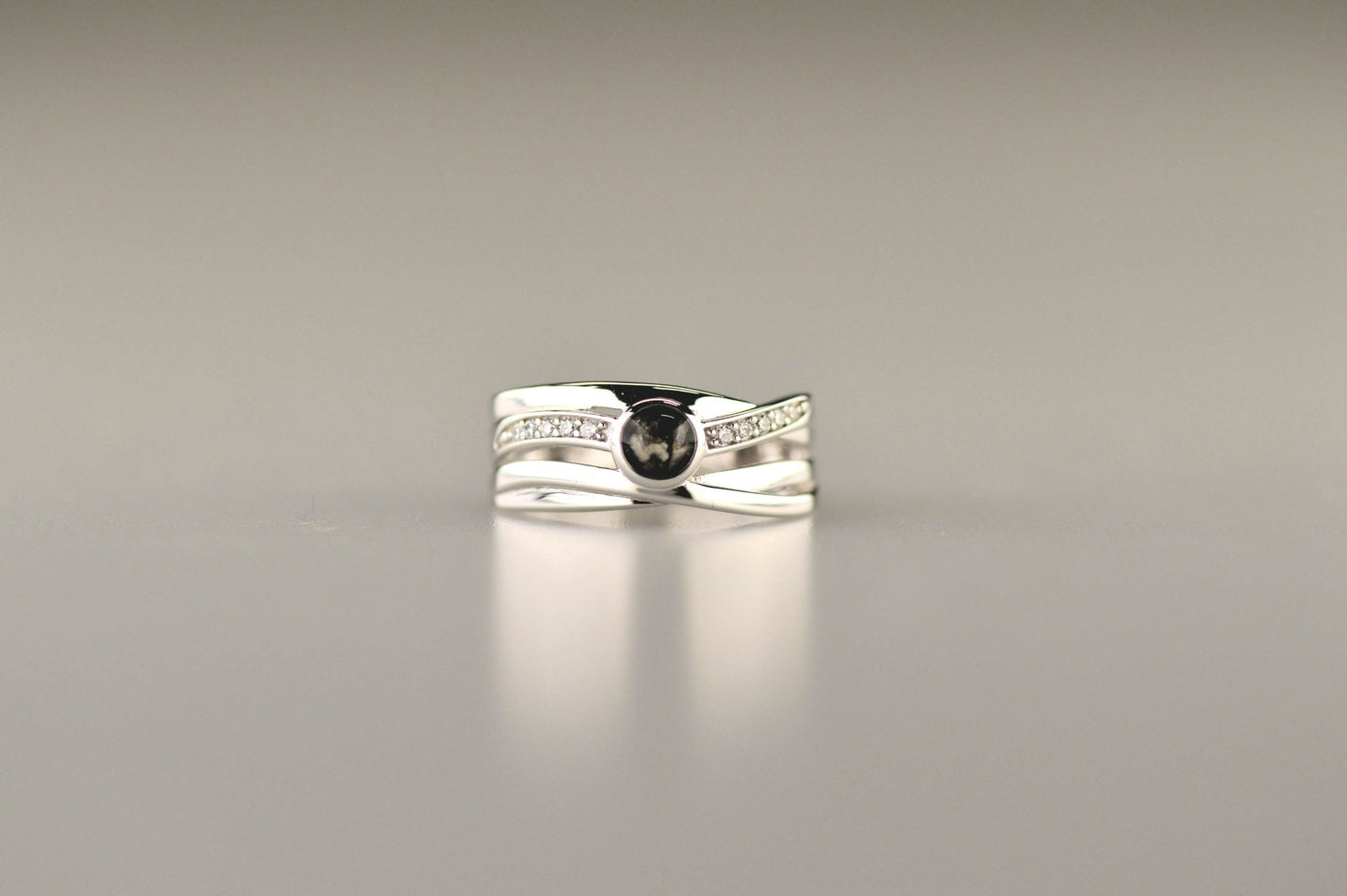 Gedenksieraad, creatieve ring 9 mm breed waar aan de bovenzijde zichtbaar as of haar verwerkt wordt in een deel van de ringband, een andere band is gezet met zirkonia's of diamanten naar keuze. Alle