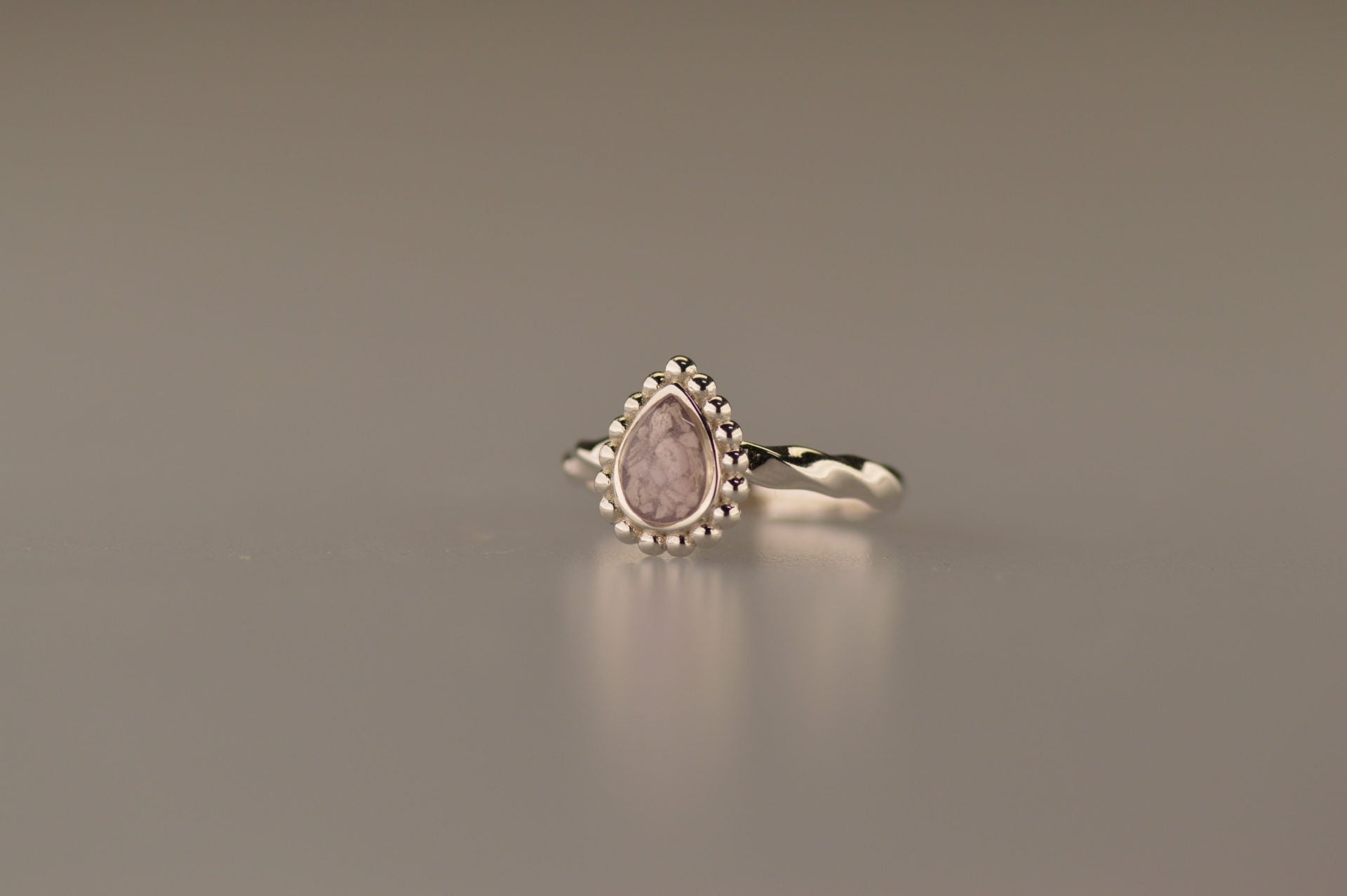 Gedenksieraad, asring met gedraaide scheen waar aan de bovenzijde in druppelvorm met parelrand zichtbaar as of haar (of eventueel melktandjes of moedermelk) verwerkt wordt.alle