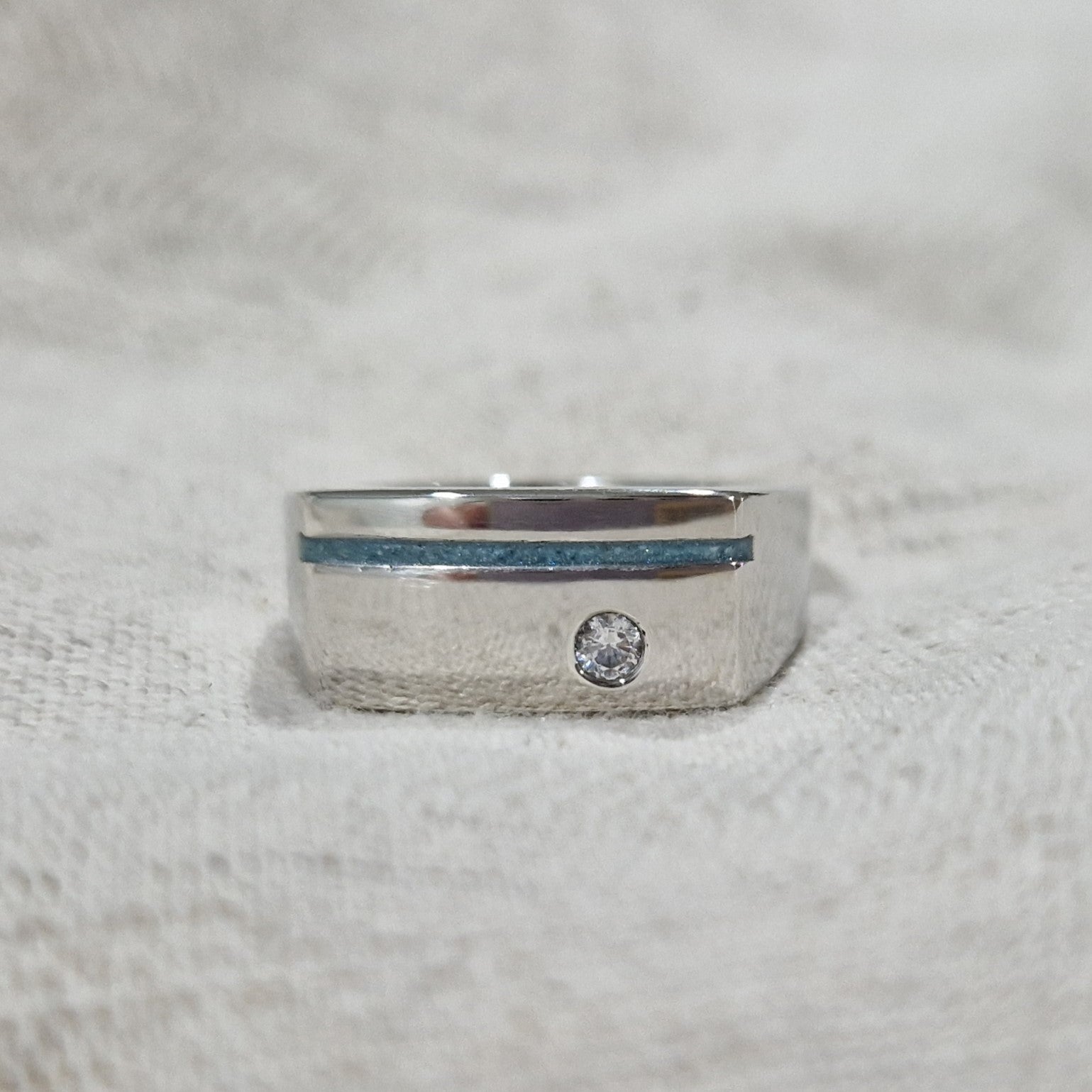 Ring als gedenksieraad met een streep aan de voorzijde, waar as of haar  in verwerkt wordt. Ernaast is een zirkonia gezet. Alle