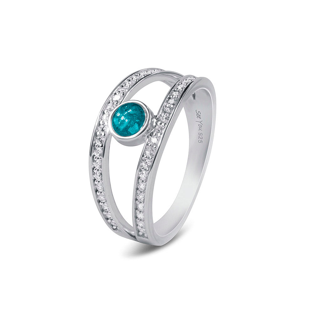 Gedenksieraad, ring waar aan de bovenzijde zichtbaar as of haar verwerkt wordt. In de bovenste helft van de ringband zijn subtiel edelstenen naar keuze gezet. Turquoise