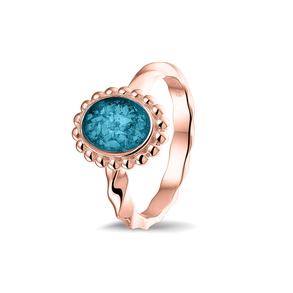 Gedenksieraad, asring met gedraaide scheen waar aan de bovenzijde in druppelvorm met parelrand zichtbaar as of haar (of eventueel melktandjes of moedermelk) verwerkt wordt. Turquoise