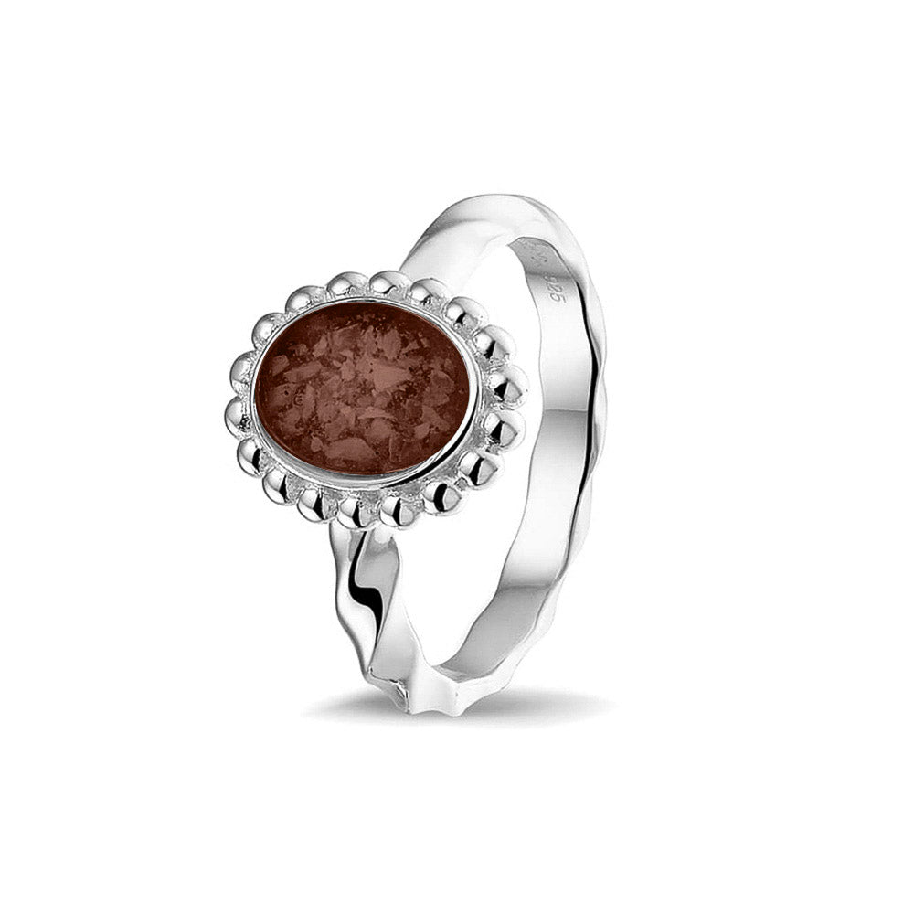 Gedenksieraad, asring met gedraaide scheen waar aan de bovenzijde in druppelvorm met parelrand zichtbaar as of haar (of eventueel melktandjes of moedermelk) verwerkt wordt. Brown