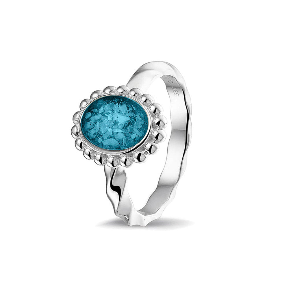 Gedenksieraad, asring met gedraaide scheen waar aan de bovenzijde in druppelvorm met parelrand zichtbaar as of haar (of eventueel melktandjes of moedermelk) verwerkt wordt. Turquoise