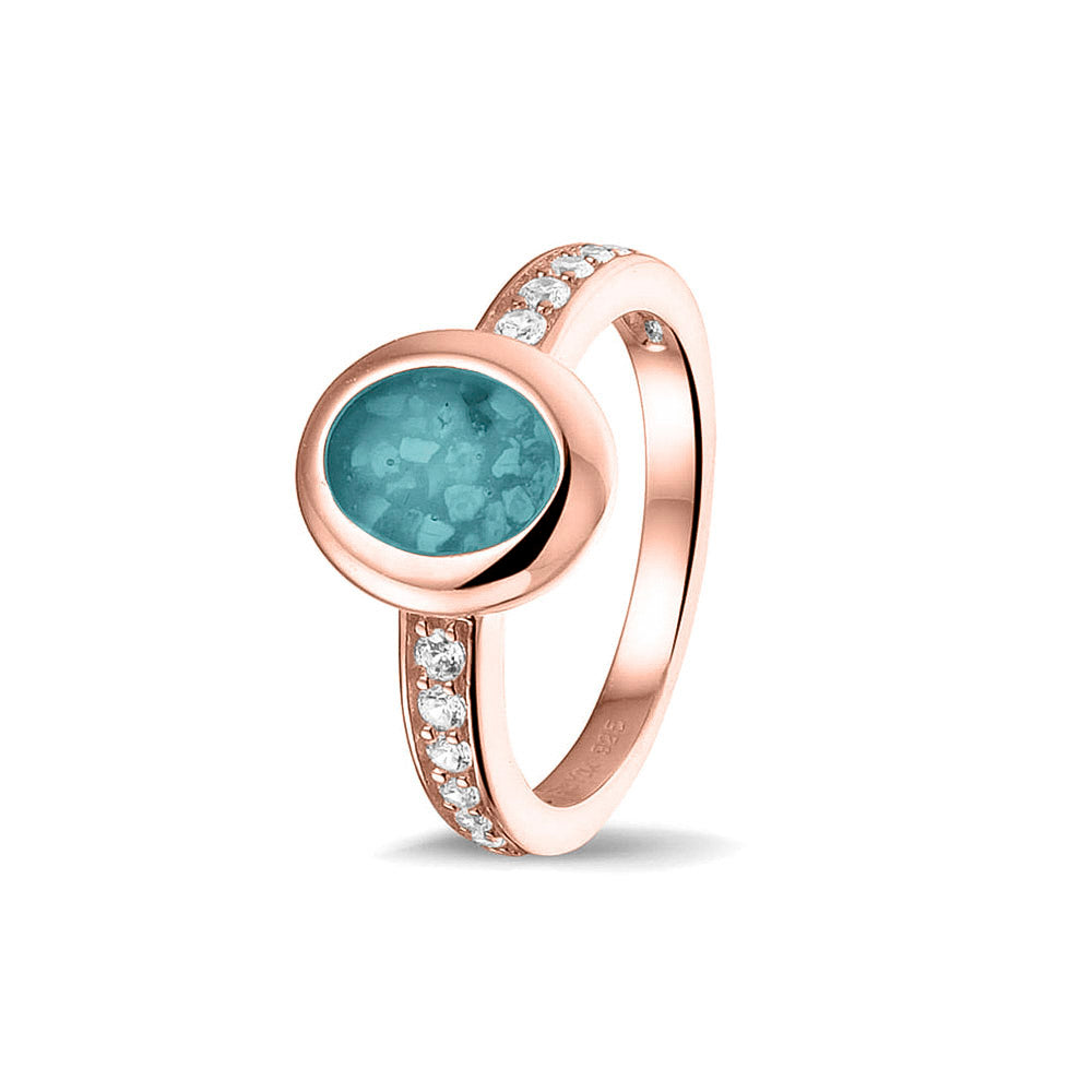 Gedenksieraad, ring 3 mm waar aan de ovale bovenzijde zichtbaar as of haar verwerkt wordt. In de bovenste helft van de ringband zijn zirkonia's of diamanten naar keuze gezet. Aqua
