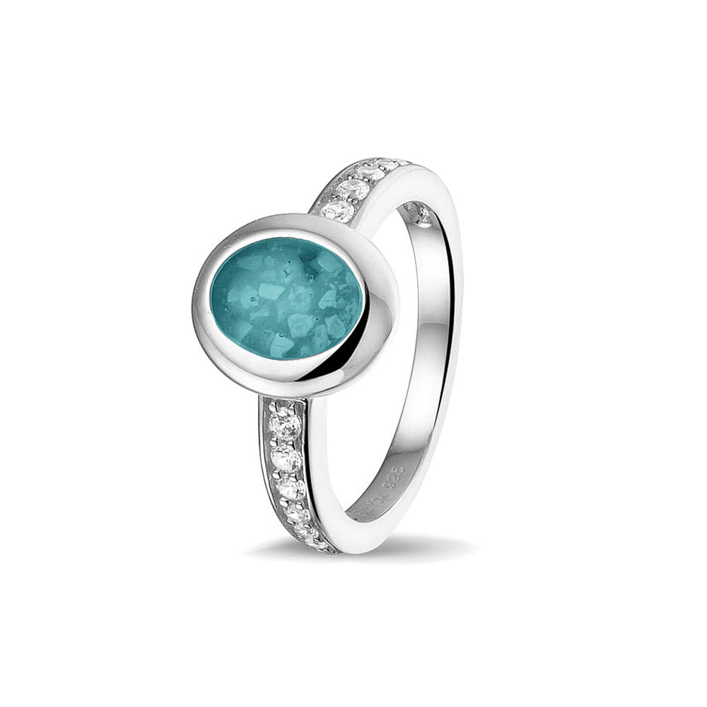 Gedenksieraad, ring 3 mm waar aan de ovale bovenzijde zichtbaar as of haar verwerkt wordt. In de bovenste helft van de ringband zijn zirkonia's of diamanten naar keuze gezet. Aqua