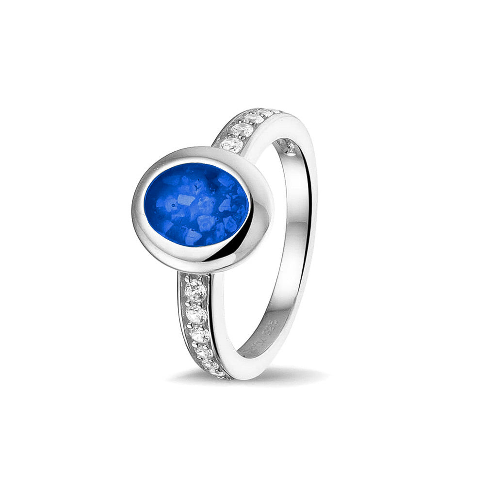 Gedenksieraad, ring 3 mm waar aan de ovale bovenzijde zichtbaar as of haar verwerkt wordt. In de bovenste helft van de ringband zijn zirkonia's of diamanten naar keuze gezet. Blue