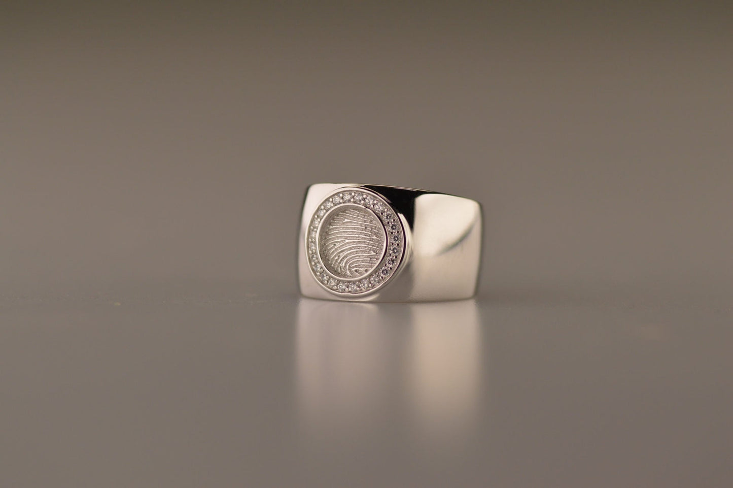 Ring met rond vlak aan de bovenzijde voorzien van een vingerafdruk afgewerkt aan de randen met diamanten. alle