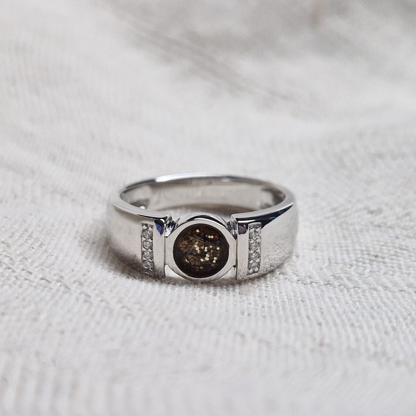Ring 6 mm uit onze serie gedenksieraden, waar zichtbaar as of haar verwerkt wordt in het ronde ornament geflankeerd door acht stuks zirkonia's of diamanten naar keuze. Alle