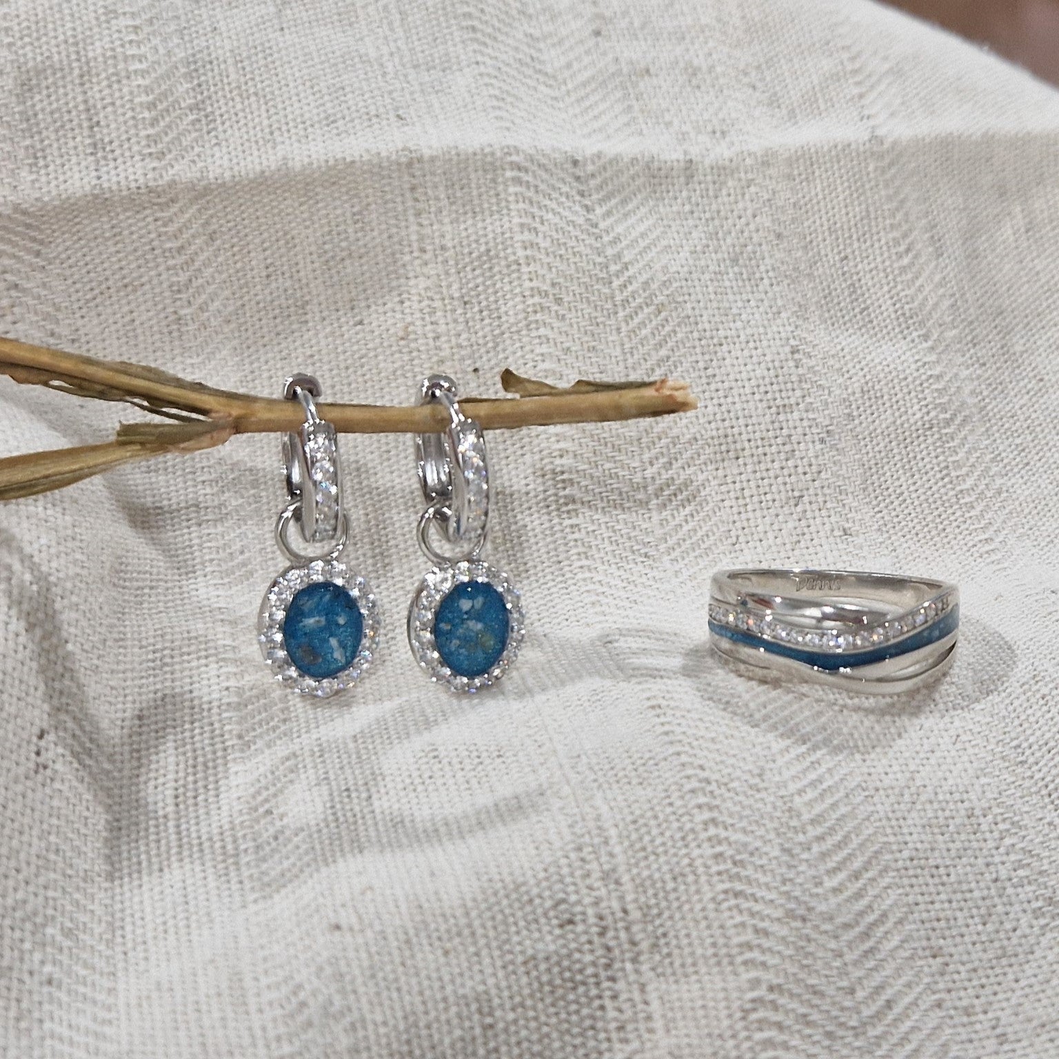 Ovaal gevormde oorhangers, 18 mm lang rondom afgewerkt met zirkonia's, aan de voorzijde zichtbaar gevuld met as of haar. Alle