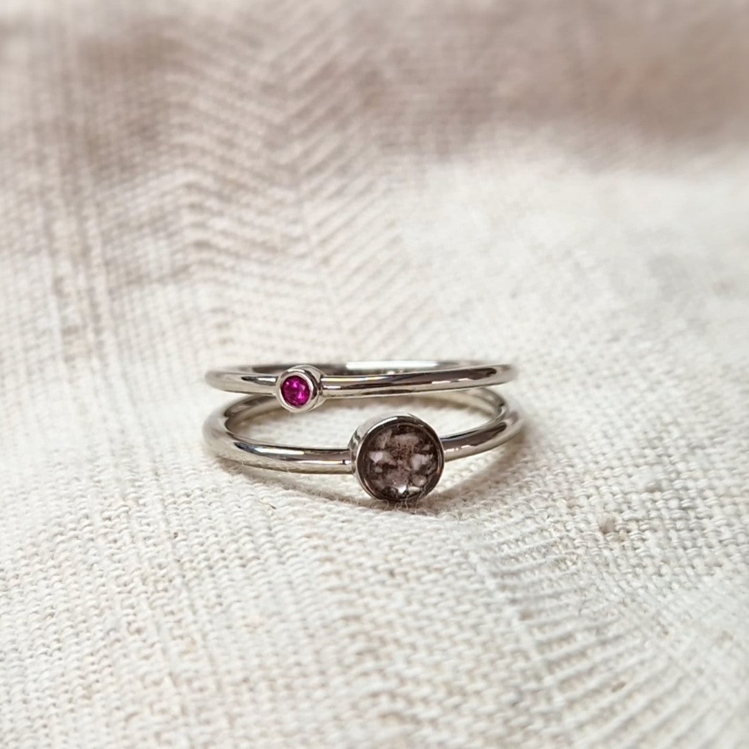 Gedenksieraad waarin een geboortesteen geplaatst wordt naar keuze. Het grotere ronde compartiment van 6 mm wordt zichtbaar gevuld met as,haar of moedermelk. Alle