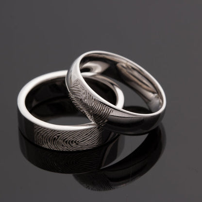 Deze asring van 6 mm breedte met vingerafdruk is heeft een subtiel weggewerkt askamertje, waar een symbolische hoeveelheid as of haar in kan bewaard worden. Alle