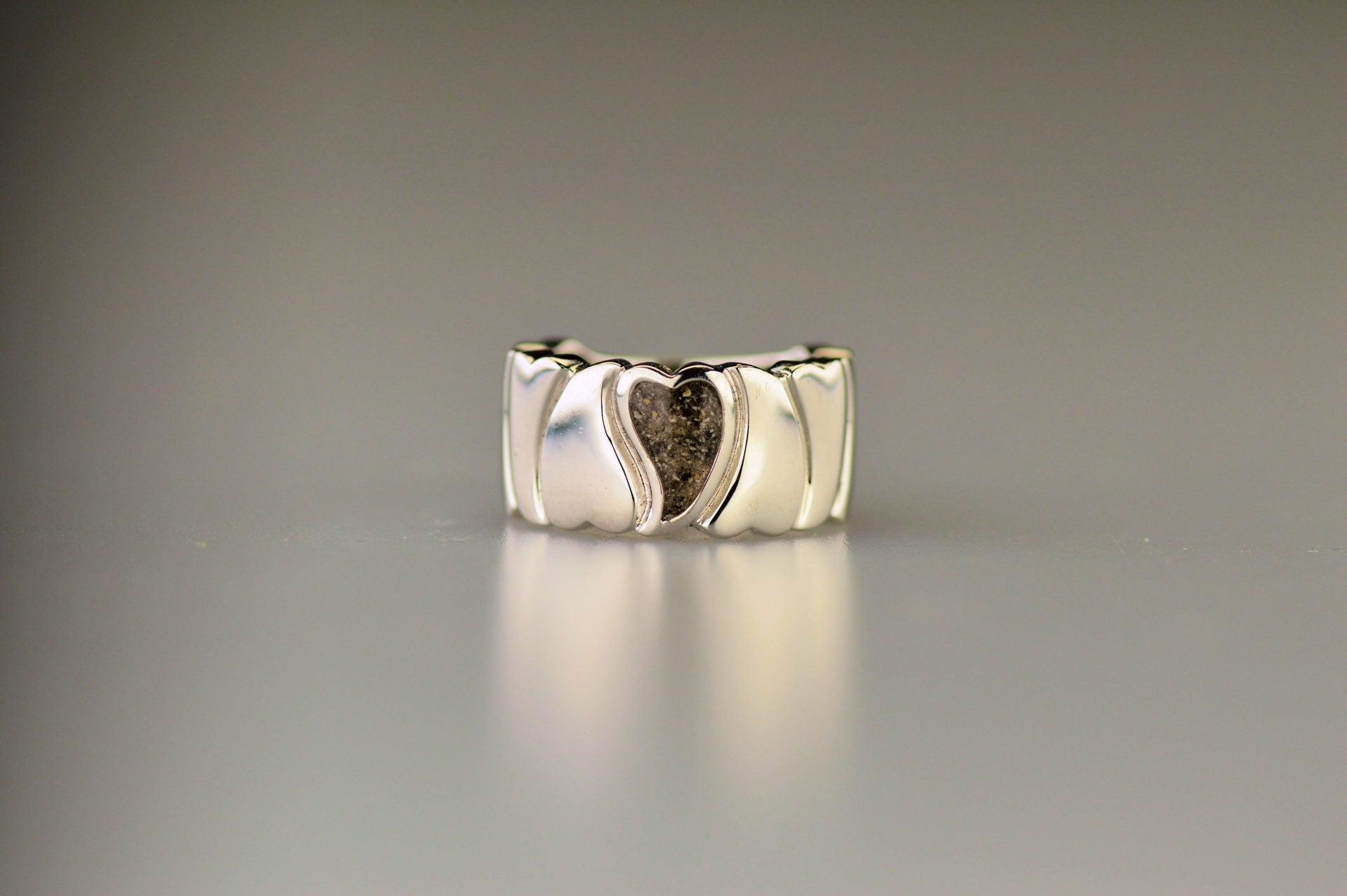 Ring 12 mm uit onze serie gedenksieraden, waar aan de bovenzijde zichtbaar as of haar (of eventueel melktandjes of moedermelk) verwerkt wordt in een hartje. 