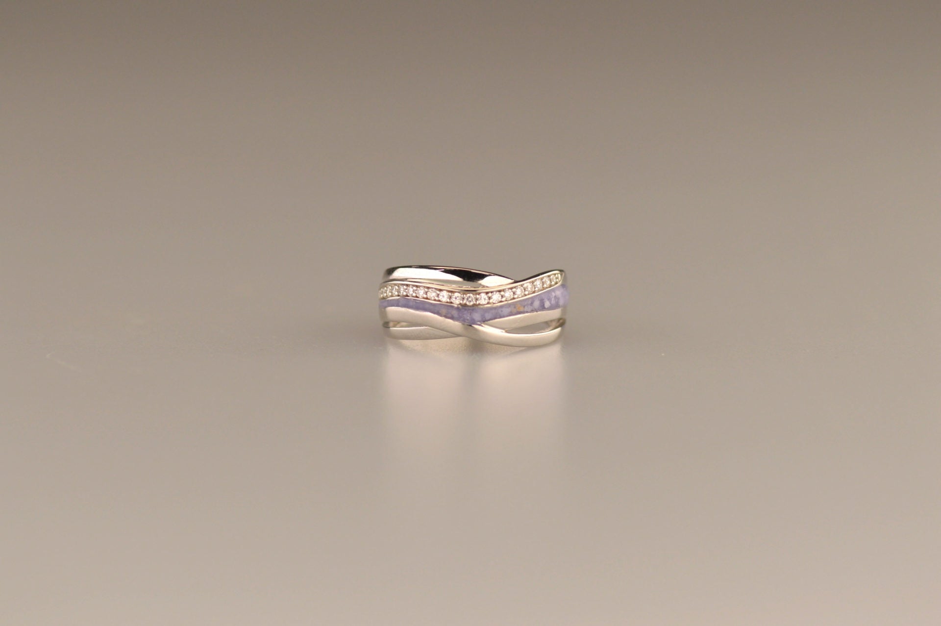 Gedenksieraad, creatieve ring 8 mm waar aan de bovenzijde zichtbaar as of haar verwerkt wordt in een deel van de ringband, een andere band is gezet met zirkonia's of diamanten naar keuze.  De asring is leverbaar in zilver en in 14 en 18 KT geelgoud/witgoud en roségoud.