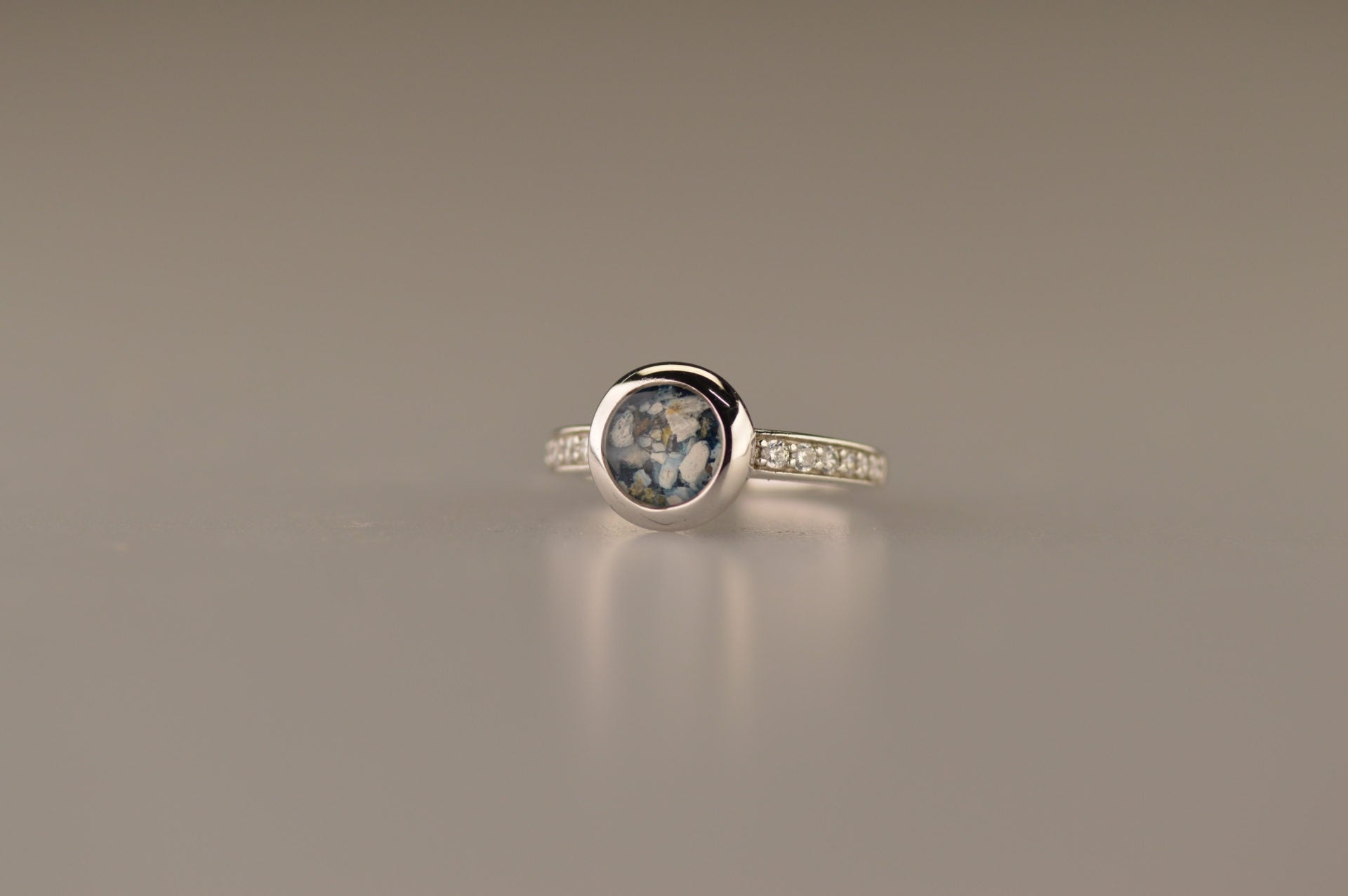 Gedenksieraad, ring 3 mm waar aan de bovenzijde zichtbaar as of haar verwerkt wordt. In de bovenste helft van de ringband zijn zirkonia's of diamanten naar keuze gezet. 