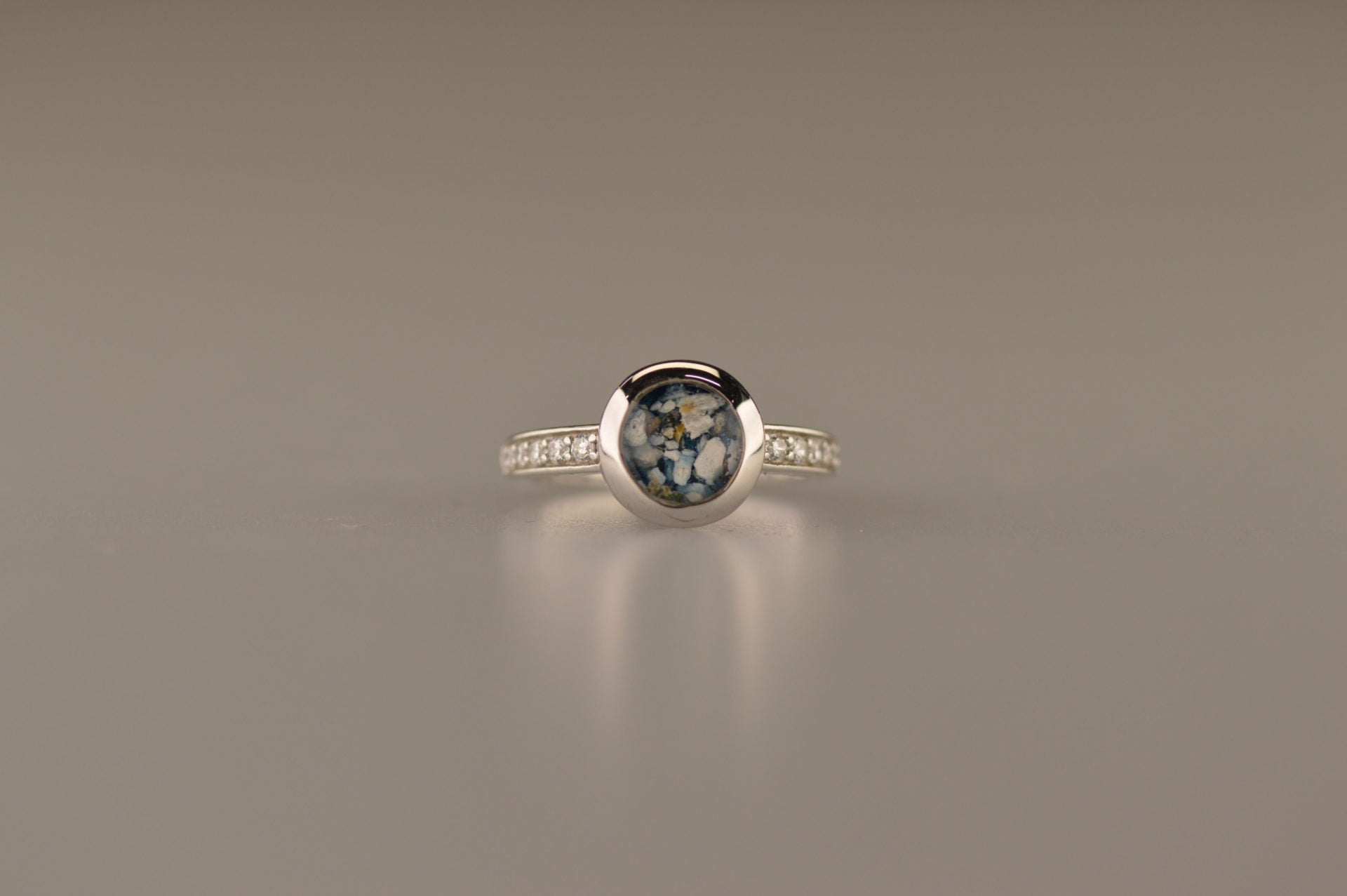 Gedenksieraad, ring 3 mm waar aan de bovenzijde zichtbaar as of haar verwerkt wordt. In de bovenste helft van de ringband zijn zirkonia's of diamanten naar keuze gezet. 