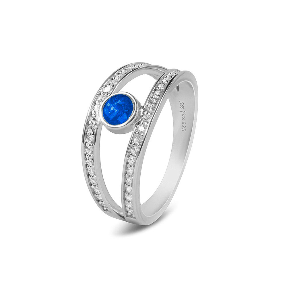 Gedenksieraad, ring waar aan de bovenzijde zichtbaar as of haar verwerkt wordt. In de bovenste helft van de ringband zijn subtiel edelstenen naar keuze gezet. Blue