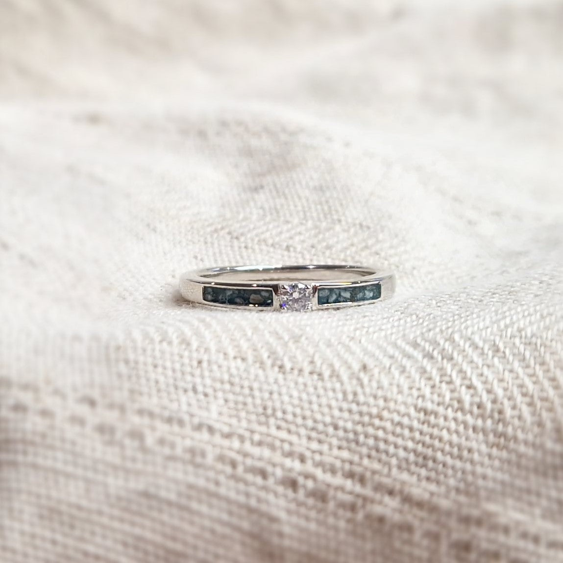Gedenksieraad, ring 3 mm met (zirkonia of diamant), geflankeerd door twee compartimenten waar zichtbaar as of haar  in verwerkt wordt. Alle